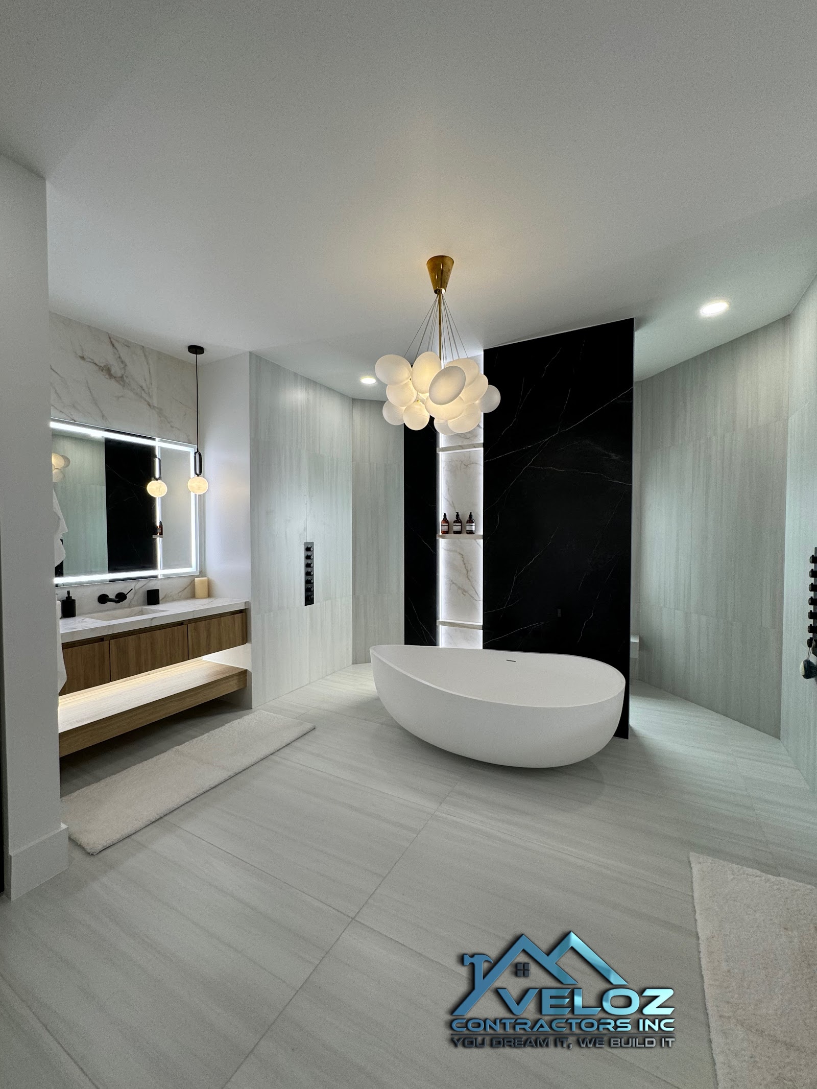 Luxury spa-like bathroom with freestanding tub, black marble feature wall, and bubble chandelier by Veloz Contractors